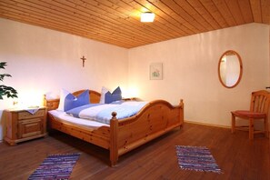 Ein Schlafzimmer mit einem hölzernen Bett, einem Nachttisch, einem Stuhl, einem Spiegel und einem Kreuz an der Wand.