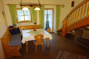 Un coin repas accueillant avec une table en bois, des chaises et un banc. On aperçoit un escalier au fond.