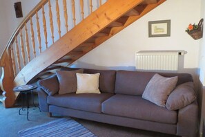 Ein Wohnzimmer mit einem braunen Sofa, einer Holztreppe, einer Heizung und einem kleinen Tisch.