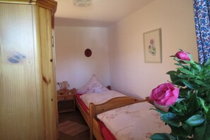 Ein Schlafzimmer mit einem Holzschrank, einem Bett mit floralem Bettzeug, einem Nachttisch und einer Topfpflanze.