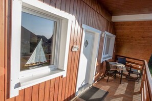A wooden deck with a table and chairs, a small sailboat model in a window, and a door with a diamond-shaped window. - Holiday apartment with 1 bedroom (Karlshagen)
