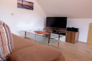 A living room with a glass-top coffee table, a flat-screen TV, and a wooden cabinet. - Holiday apartment with 1 bedroom (Karlshagen)