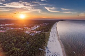 An aerial view of a coastal area with a beach, a dense forested area, and a large body of water. - Holiday apartment with 1 bedroom (Karlshagen)