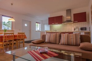 A modern living room with a glass coffee table, a sofa with striped cushions, and a dining area with wooden chairs and a red tablecloth. - Holiday apartment with 1 bedroom (Karlshagen)
