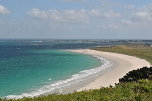 Un paysage côtier avec une plage de sable, des eaux bleues et limpides, et des bâtiments situés au loin.