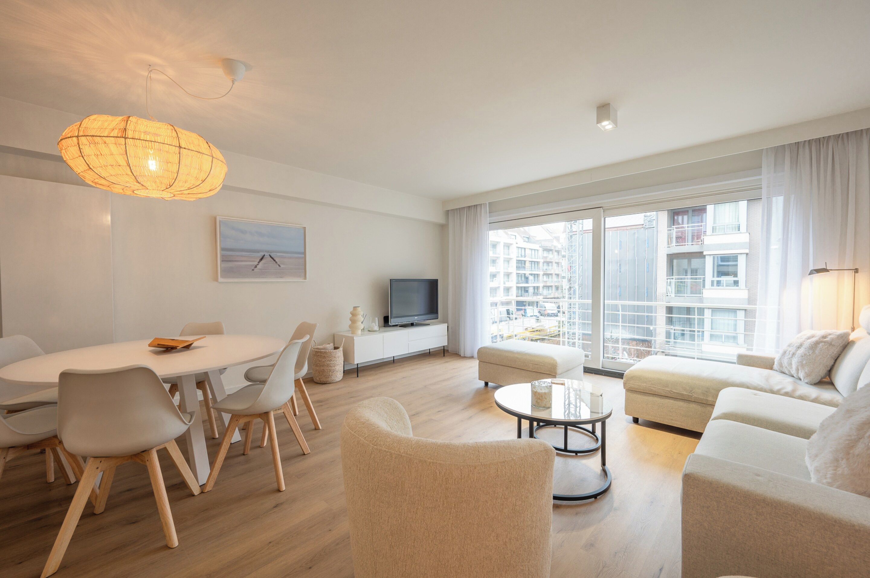 A modern living room with a dining area, a television, and large windows offering a city view.