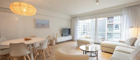 Una sala de estar moderna con comedor, televisor y ventanas amplias con vistas a la ciudad.