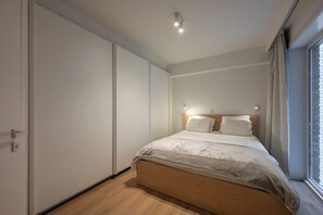 A bedroom with a bed, a wardrobe, and a window. - Central Apartment Near Rubensplein Beach (Knokke-Heist)
