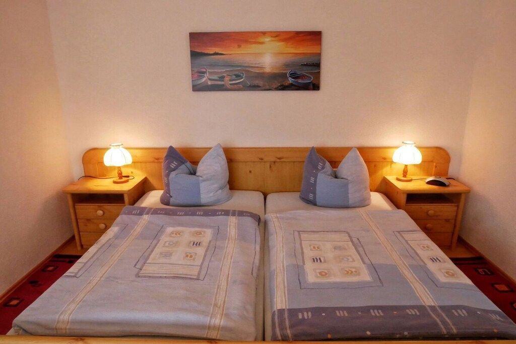 A double bed with a headboard, two bedside tables with lamps, and a painting of boats on water above the bed.