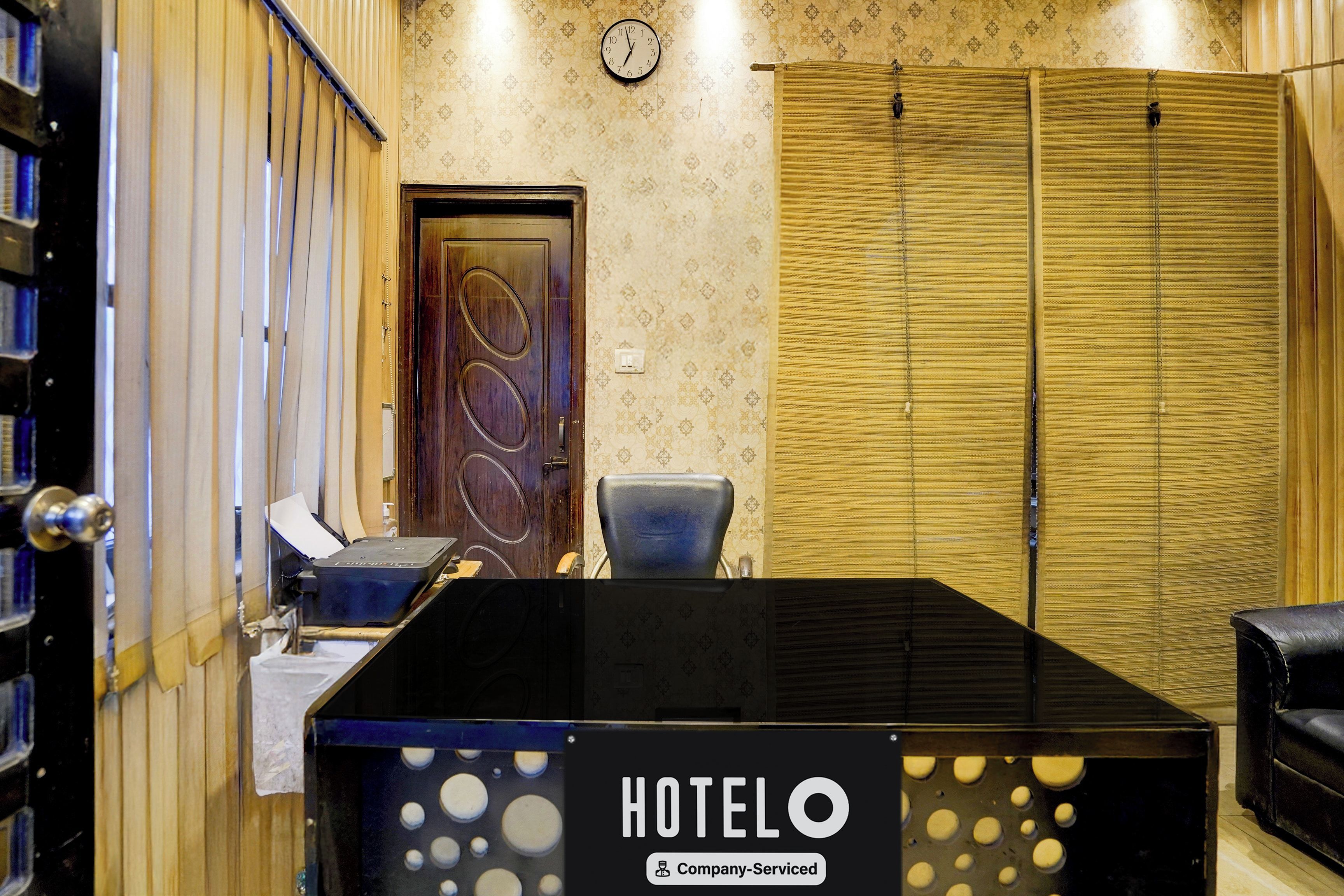 Una habitación de hotel con una minibar negra, una puerta de madera, un reloj en la pared y un papel tapiz estampado.