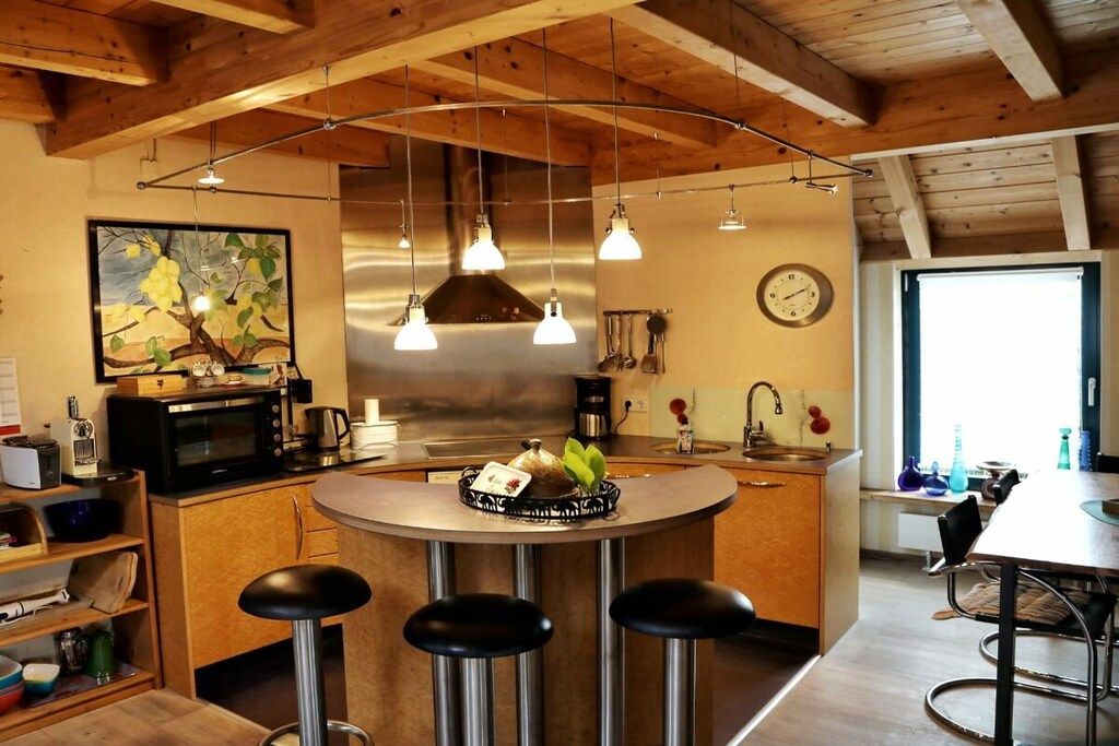 Una cucina con isola centrale, sgabelli da bar, lampade a sospensione, un orologio e una finestra.