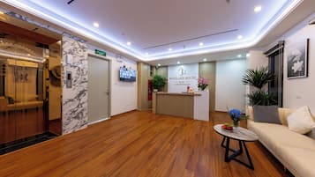 Zona de recepción de un hotel con suelo de madera, un mostrador, un sofá y una mesa de centro.
