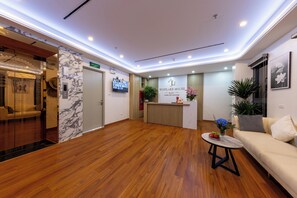 A hotel reception area with a wooden floor, a reception desk, a sofa, and a coffee table. - Westlake House by Jen (Hanoi)