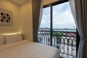 A hotel room with a bed, a window with a view of a cityscape, and a wall-mounted artwork. - Westlake House by Jen (Hanoi)
