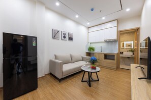 A modern living room with a sofa, a coffee table with a vase, a black refrigerator, and a kitchen area with cabinets and a sink. - Westlake House by Jen (Hanoi)