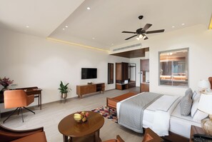 Une chambre d’hôtel moderne équipée d’un lit, d’un coin salon, d’une télévision et d’une salle de bain visible à travers une porte en verre.