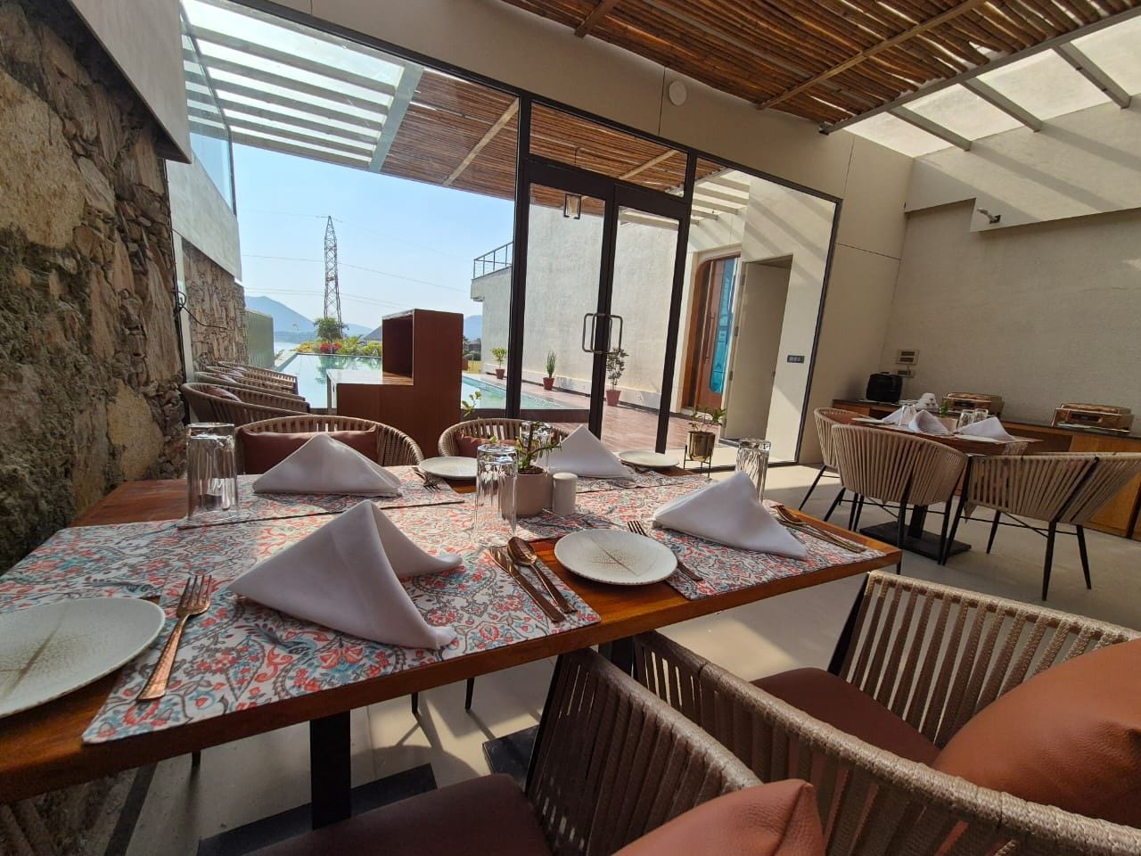 A dining area with tables set for four, outdoor seating, and a view of the mountains.