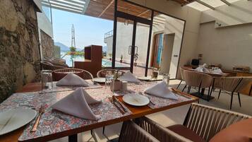 A dining area with tables set for four, outdoor seating, and a view of the mountains.