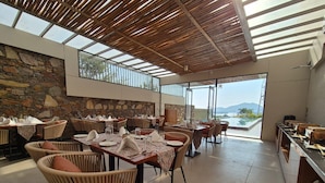 A restaurant with outdoor seating, stone walls, and a view of the mountains. - Traavista Rivera The Lake House (Panwari)