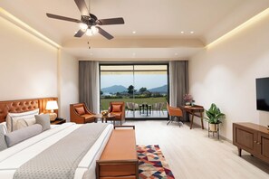 A modern hotel room with a large bed, a desk, a chair, a television, and a balcony with a view of the mountains. - Traavista Rivera The Lake House (Udaipur)