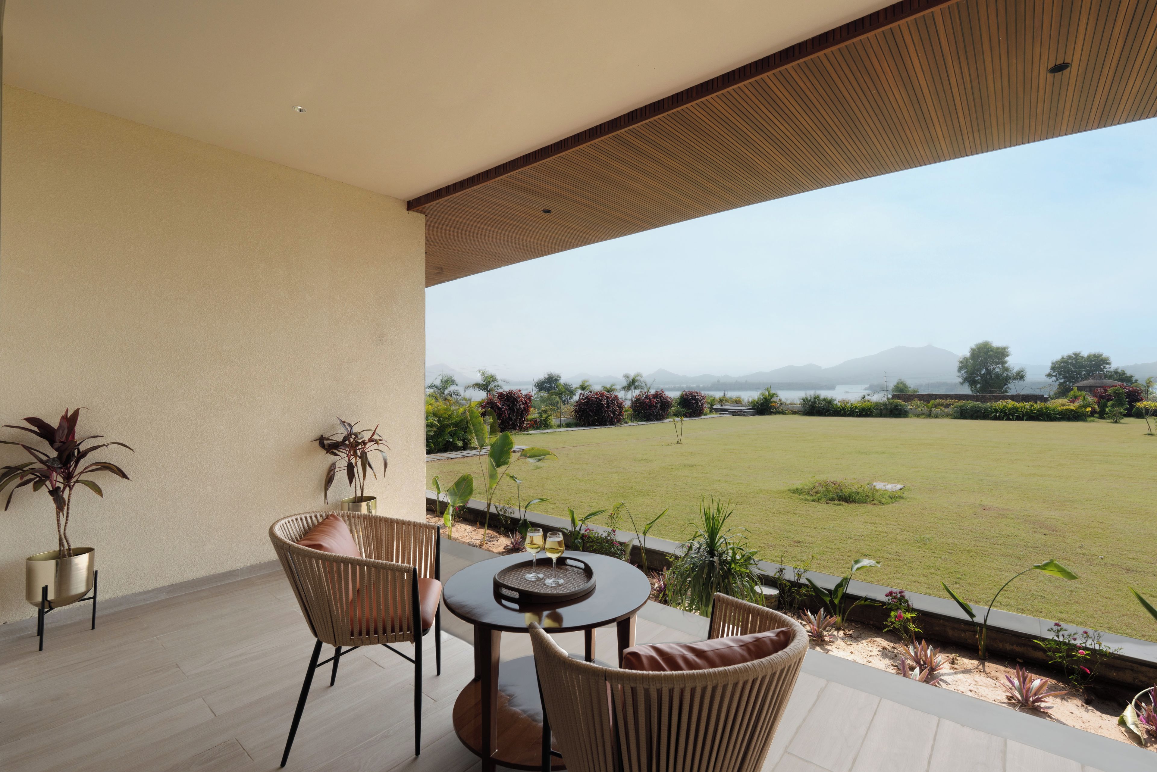 A covered outdoor seating area with wicker furniture and a view of a well-maintained lawn and distant mountains.
