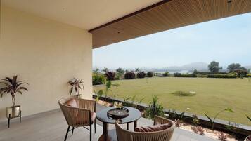 A covered outdoor seating area with wicker furniture and a view of a well-maintained lawn and distant mountains.