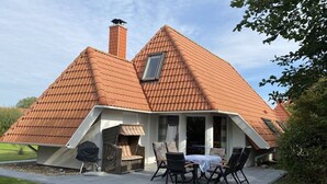 A house with a sloped roof, a chimney, and a patio with outdoor furniture. - Holiday home with 3 bedrooms (Wurster Nordseeküste)