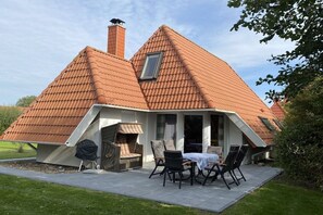 A house with a sloped roof, a chimney, and a patio with outdoor furniture. - Holiday home with 3 bedrooms (Wurster Nordseeküste)