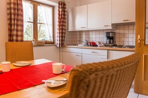 A kitchen with white cabinets, a coffee maker, and a dining area with a red tablecloth. - Haus Sprenzel - Bettina Holiday Apartment (Garmisch-Partenkirchen)