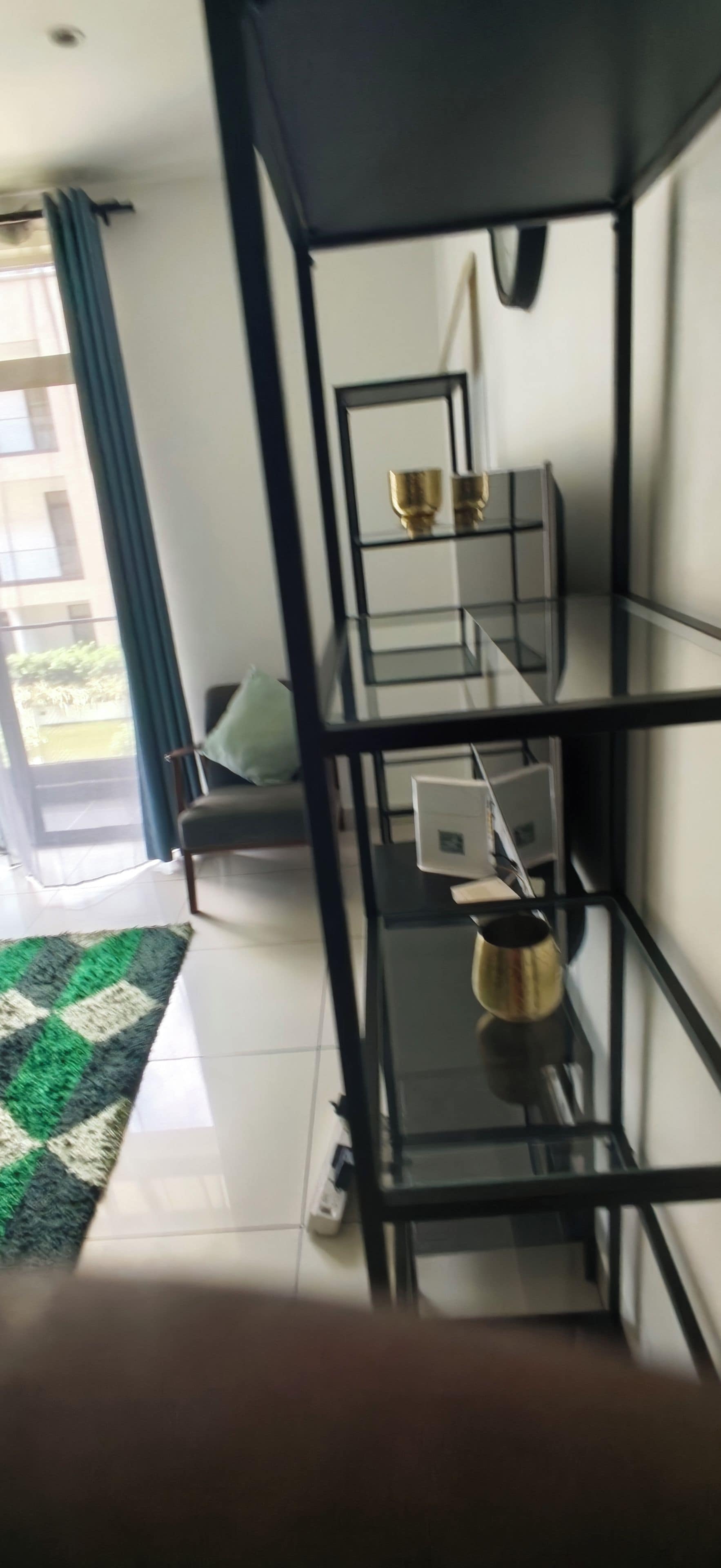 Ett modernt vardagsrum med en soffa, ett soffbord i glas och en svart hyllsektion med dekorativa föremål.