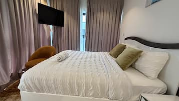 A hotel room with a bed, a television mounted on the wall, and a chair.