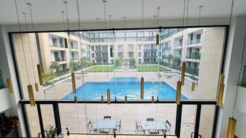 A view from a room with a large window overlooking a swimming pool and a courtyard with buildings.