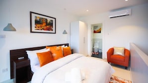 Una habitación de hotel con cama, mesita de noche, silla, armario y unidad de aire acondicionado.