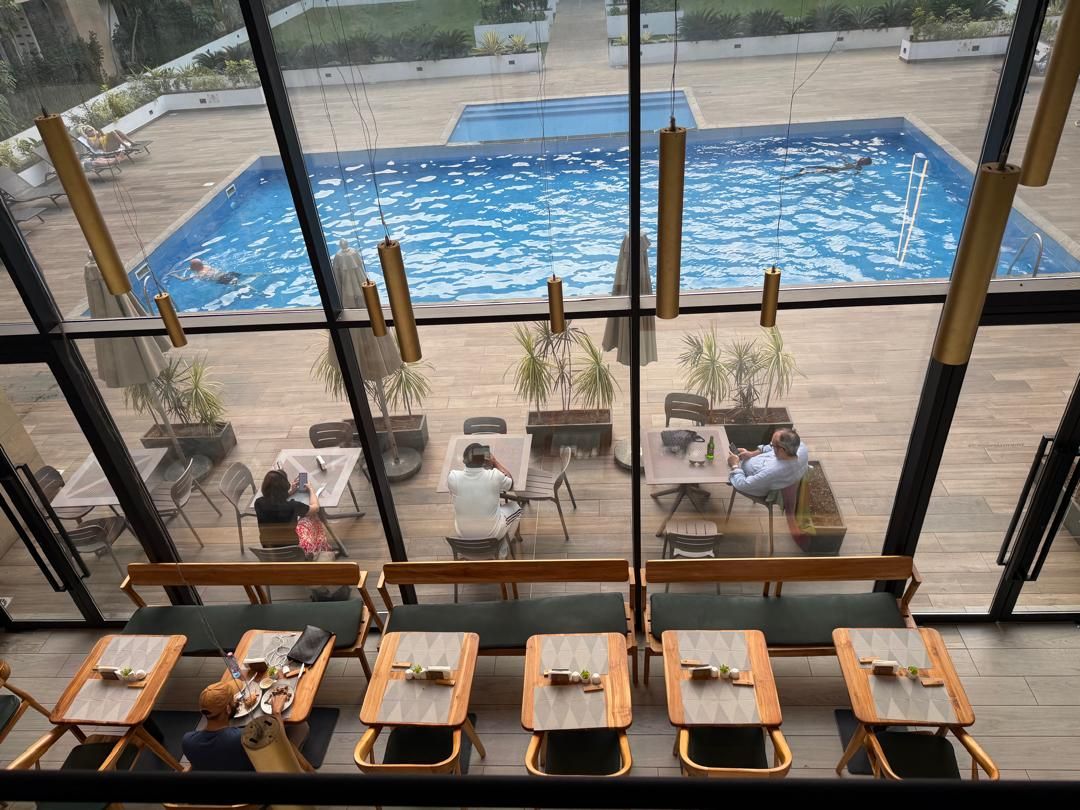 Zona junto a la piscina con mesas y sillas, una piscina y vistas de la piscina a través de amplias ventanas.