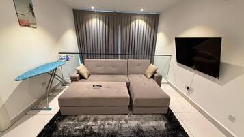 A modern living room with a sectional sofa, a flat-screen TV, and a large window with curtains.