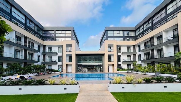 Un hotel moderno con piscina central, zona de estar al aire libre y un jardín bien cuidado.