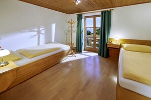 Camera d'albergo con due letti, pavimento in legno, un appendiabiti e una finestra con tende.