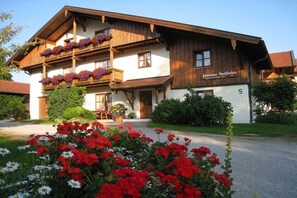 Un edificio tradizionale in legno con balconi, una targa che indica che si tratta di una pensione e un giardino curato con fiori.