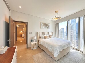 A modern hotel room with a large bed, a desk, a chair, a nightstand, a lamp, and a view of the city through large windows. - Charming 2-bedroom apartment with AC in delightful Dubai (Dubai)