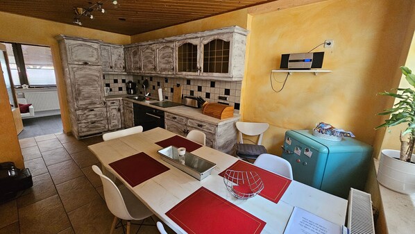 A kitchen with a dining area, a vintage-style refrigerator, and a window with blinds.