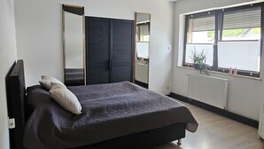 A bedroom with a bed, a small white table, a window with blinds, and a ceiling with recessed lighting. - Apartment 'HarzNest' with Private Terrace, Private Garden and Wi-Fi (Wimmelburg)