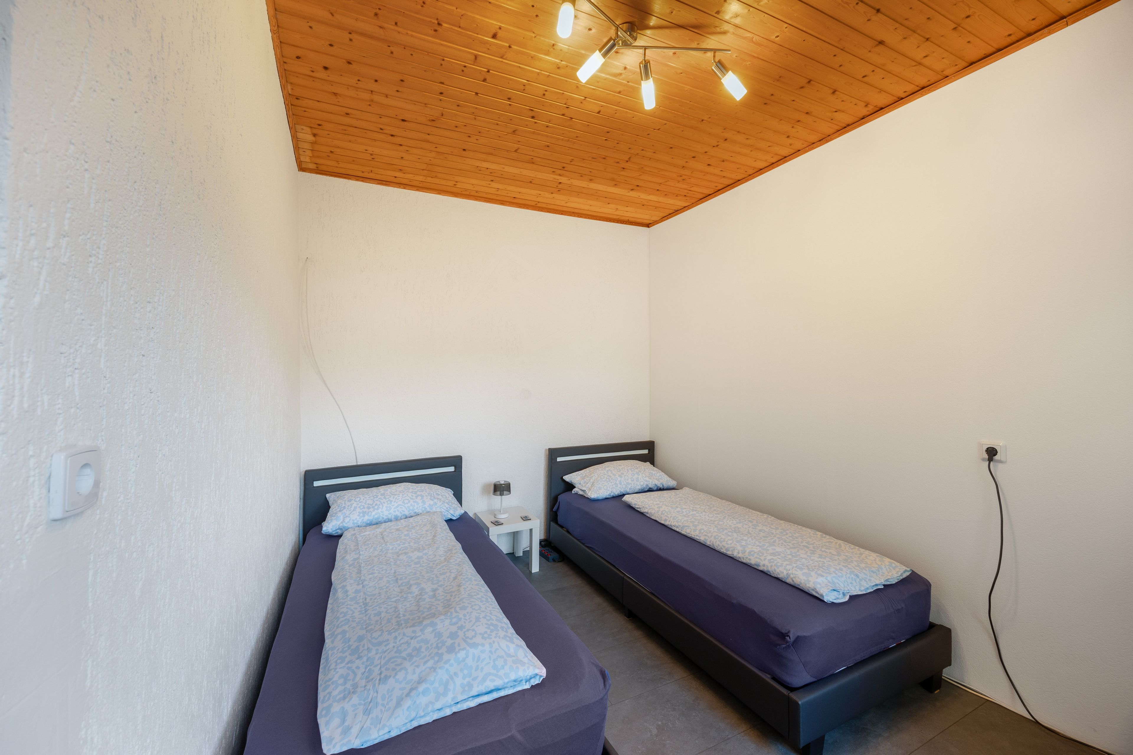Una habitación con dos camas individuales, techo de madera y pared blanca.