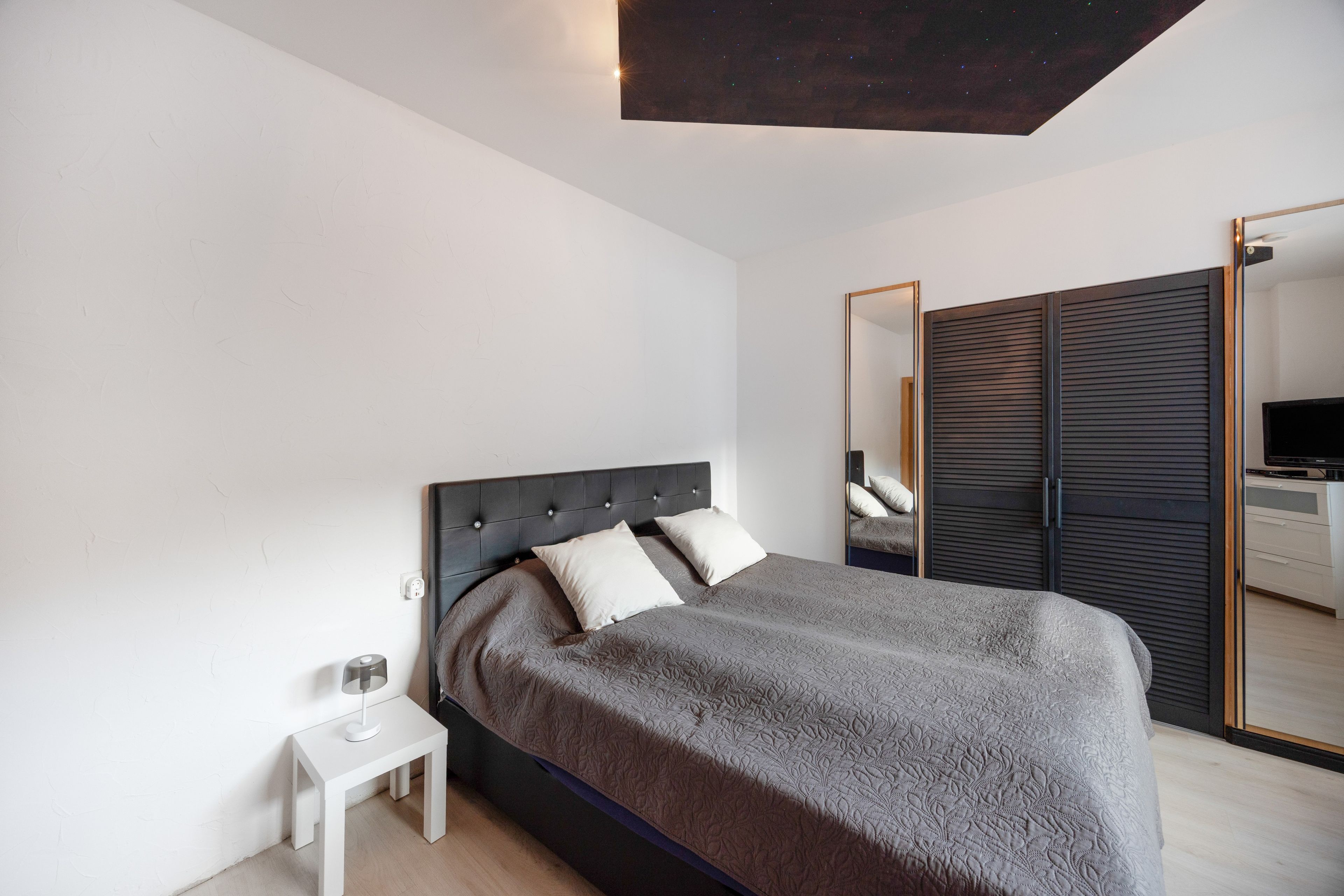 Un dormitorio moderno con cama, mesita de noche y espejo.