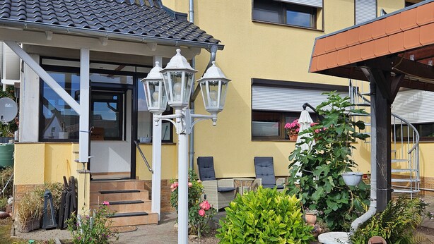 A yellow building with a tiled roof, outdoor seating, and a garden with potted plants. - Apartment 'HarzNest' with Private Terrace, Private Garden and Wi-Fi (Wimmelburg)