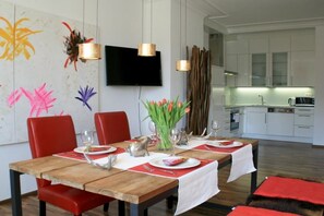 A modern dining area with a wooden table set for four, red chairs, and a kitchen in the background. - Holiday apartment with 1 bedroom (Lindau)