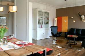 A dining area with a wooden table set for two, a white cabinet with glass doors, a black armchair, and a black sofa. - Holiday apartment with 1 bedroom (Lindau)