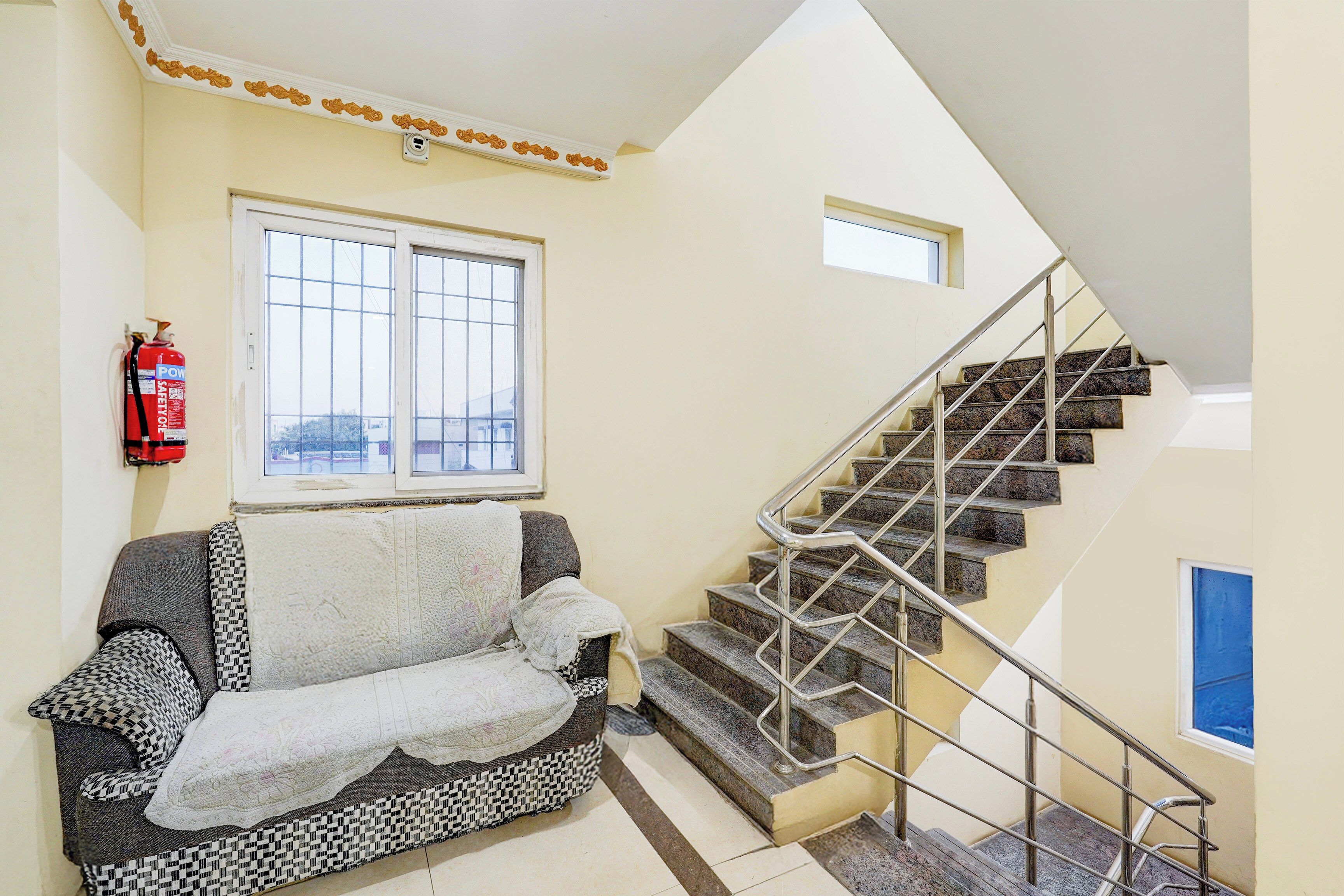 Una sala de estar con un sofá, un extintor, una ventana y una escalera.