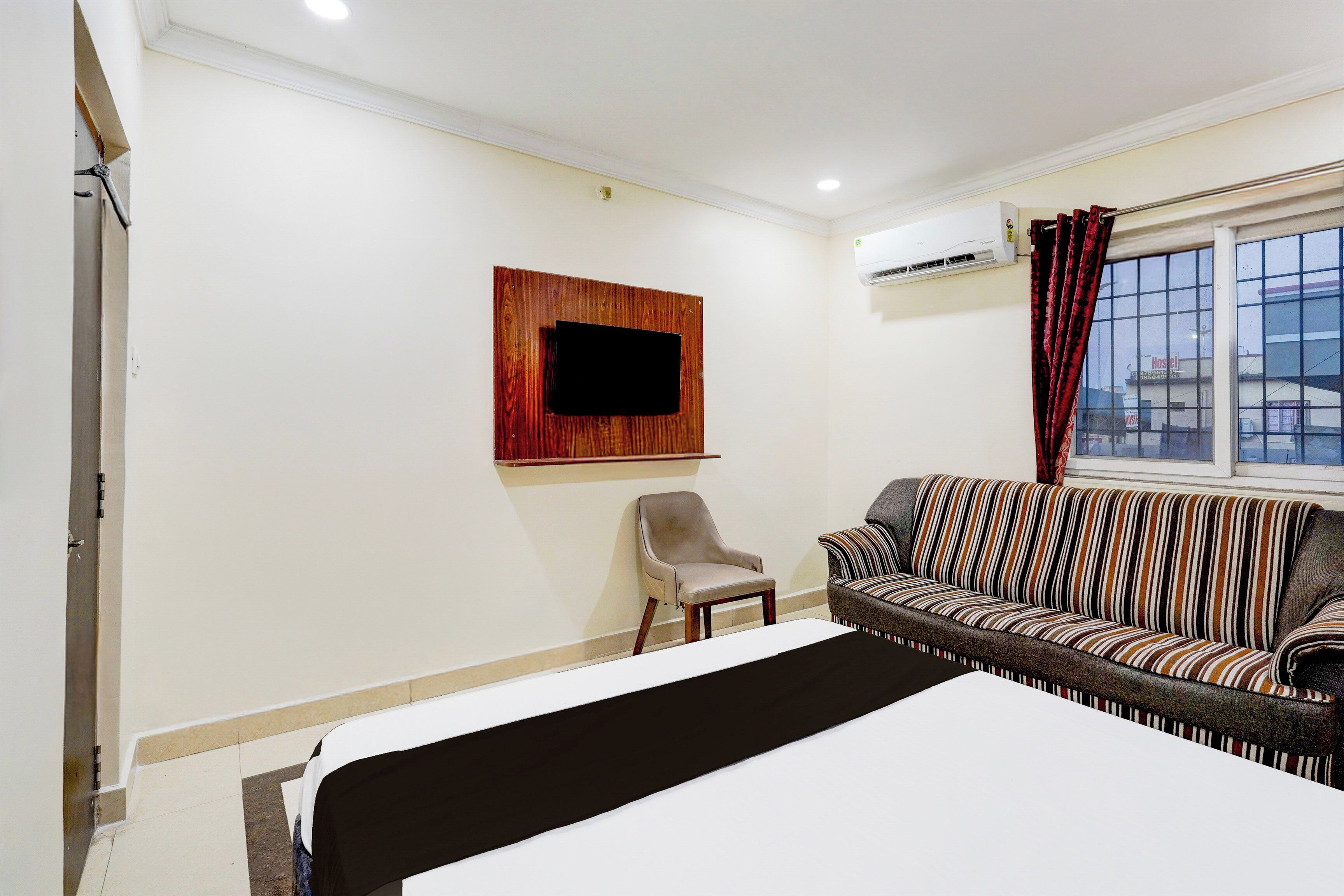 Una habitación de hotel con cama, sofá, sillón, televisor montado y aire acondicionado.