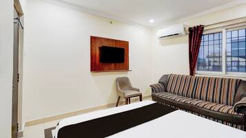 Una habitación de hotel con cama, sofá, sillón, televisor montado y aire acondicionado.