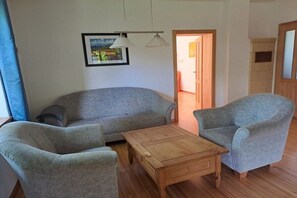 Una sala de estar con un sofá, dos sillones, una mesa de centro de madera y un cuadro en la pared.